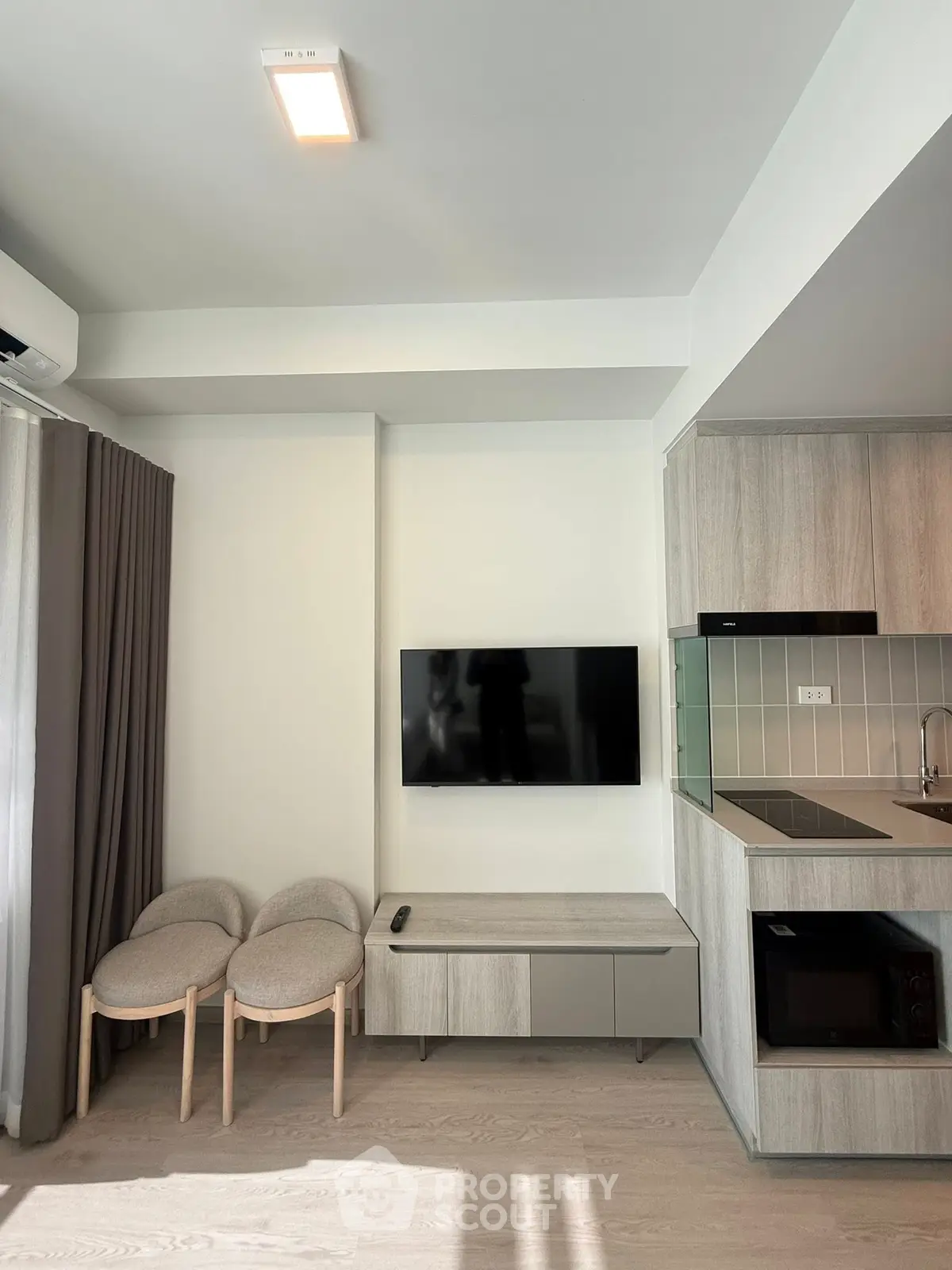 Modern living room with sleek kitchen, featuring a wall-mounted TV and stylish furniture.