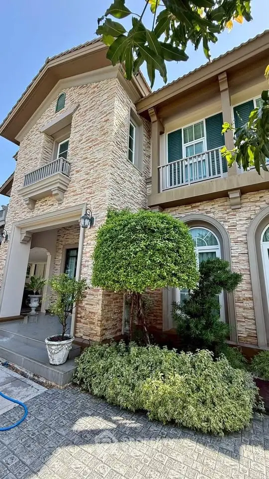 Elegant two-story stone facade house with lush greenery and stylish architecture.