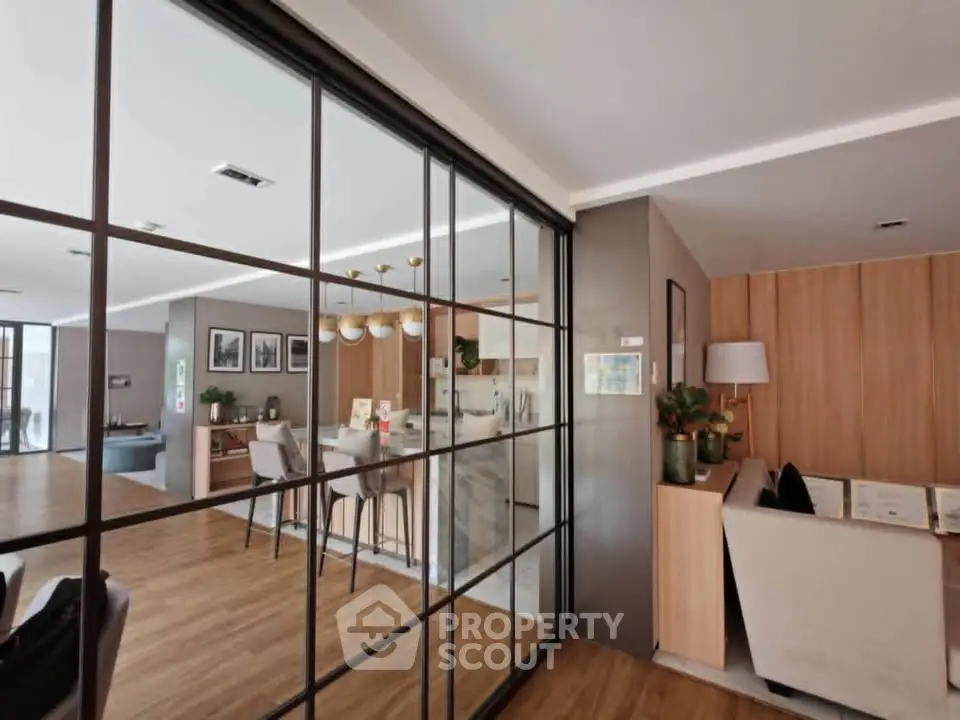Modern open-plan living room with stylish kitchen and dining area, featuring sleek glass partitions and wooden flooring.