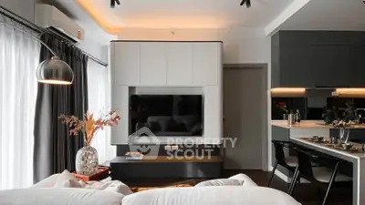 Modern living room with sleek design, featuring a wall-mounted TV, stylish lighting, and open kitchen layout.