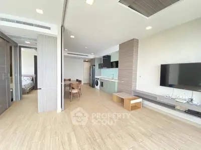 Spacious modern living room with open kitchen and dining area, featuring sleek furniture and natural lighting.
