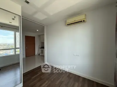 Spacious room with wooden flooring and air conditioning, featuring a large window with city views.