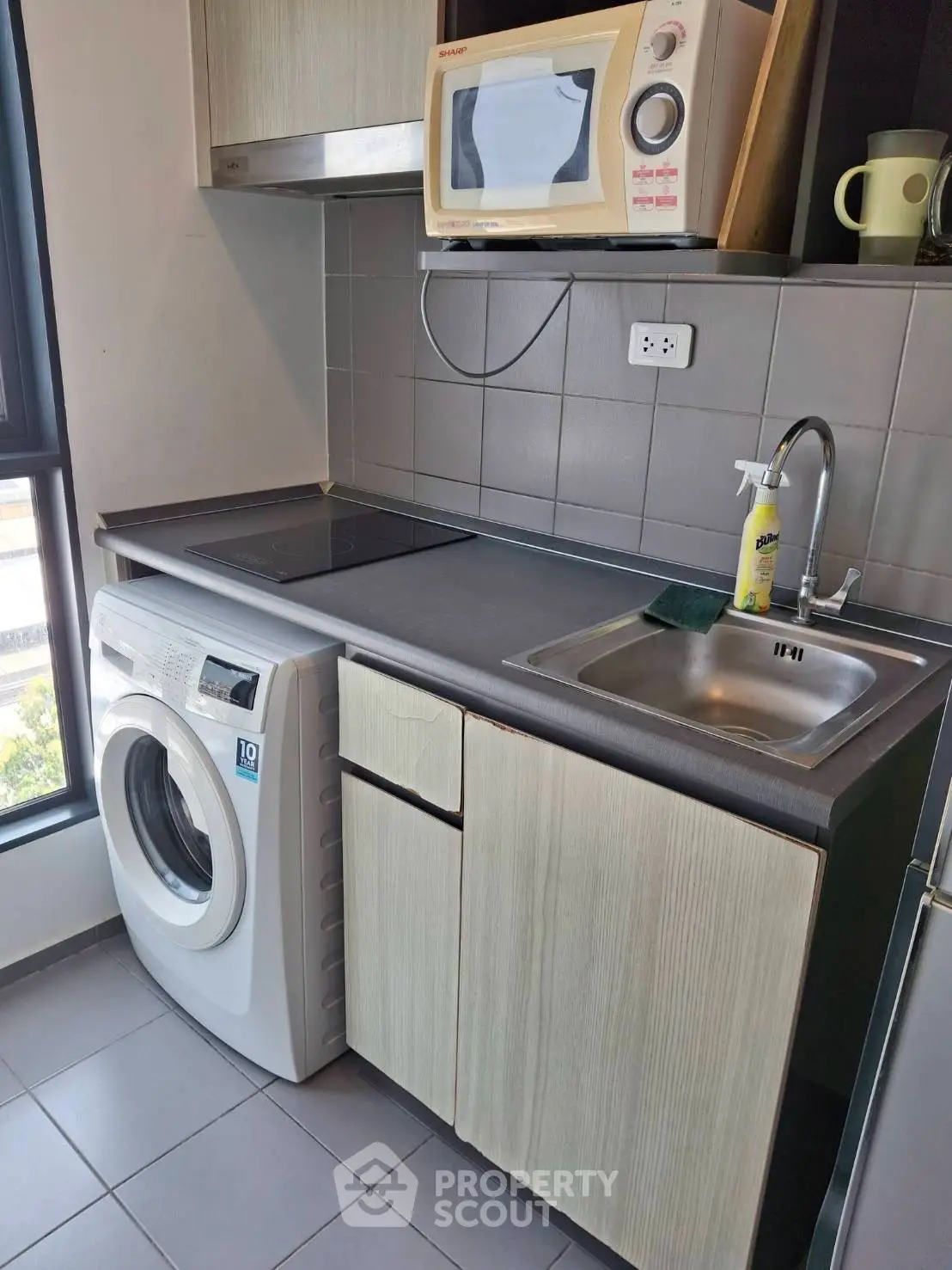 Compact kitchen with washing machine, microwave, and sink in modern apartment.