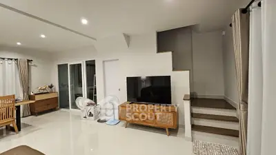 Modern living room with sleek design, featuring a flat-screen TV, wooden furniture, and elegant staircase.