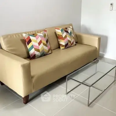 Modern living room with beige sofa and colorful pillows, complemented by a sleek glass coffee table.