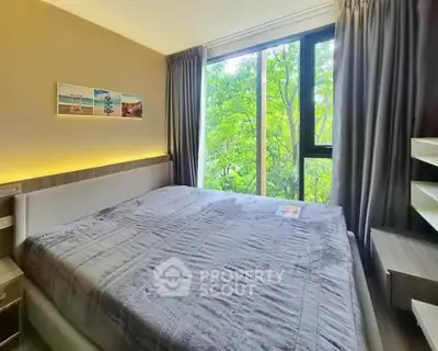 Cozy bedroom with large window and scenic view of lush greenery.