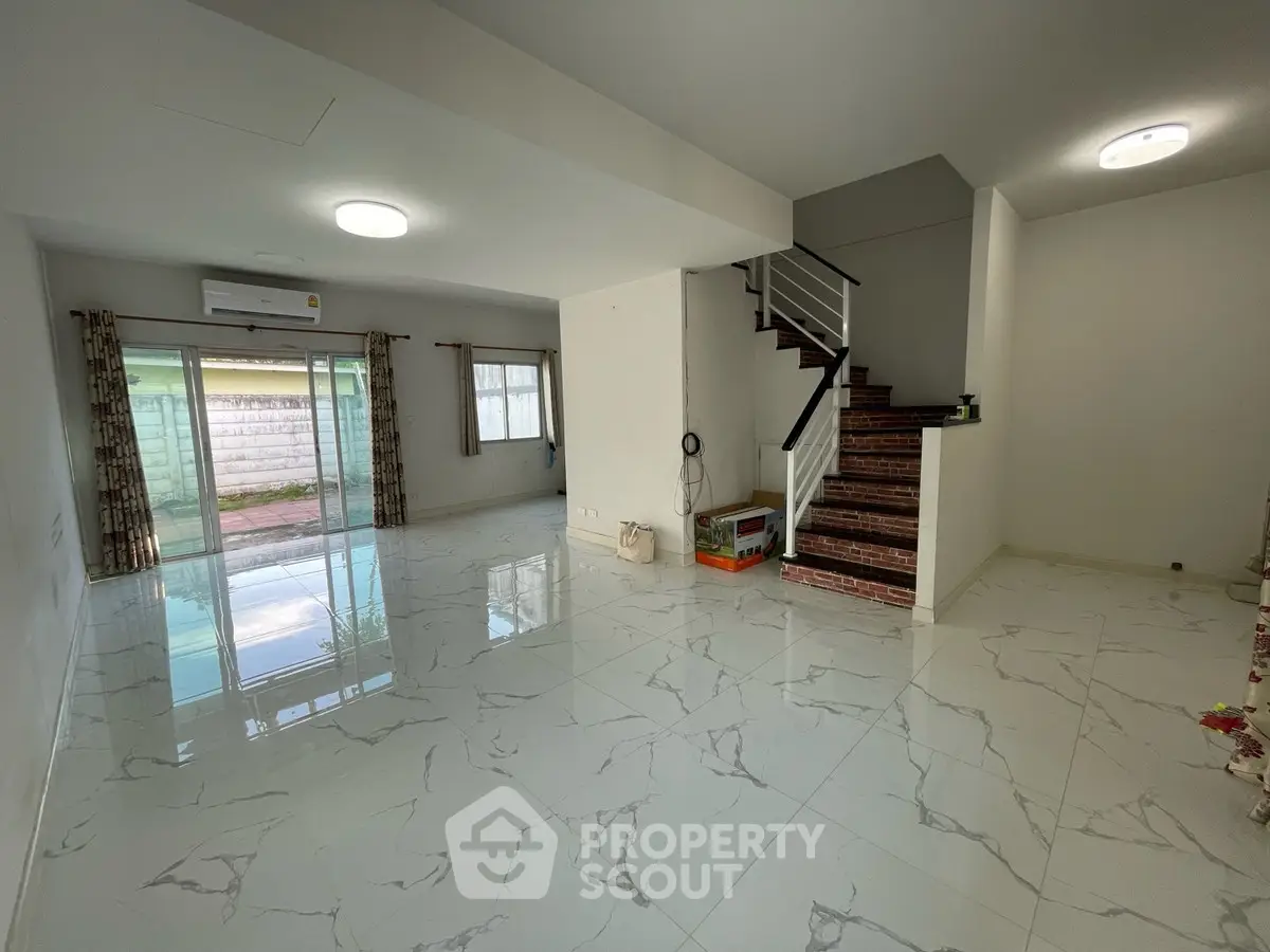 Spacious modern living room with marble flooring and staircase, featuring large windows and natural light.
