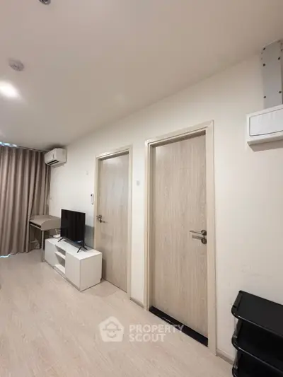 Modern apartment interior with light wood flooring, TV unit, and air conditioning.