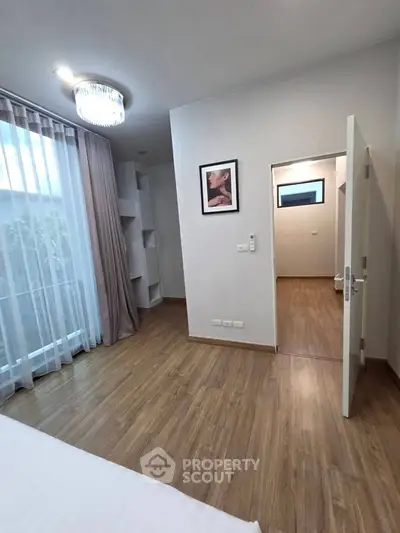 Modern bedroom with elegant lighting and wooden flooring, featuring a stylish wall art and ample natural light.