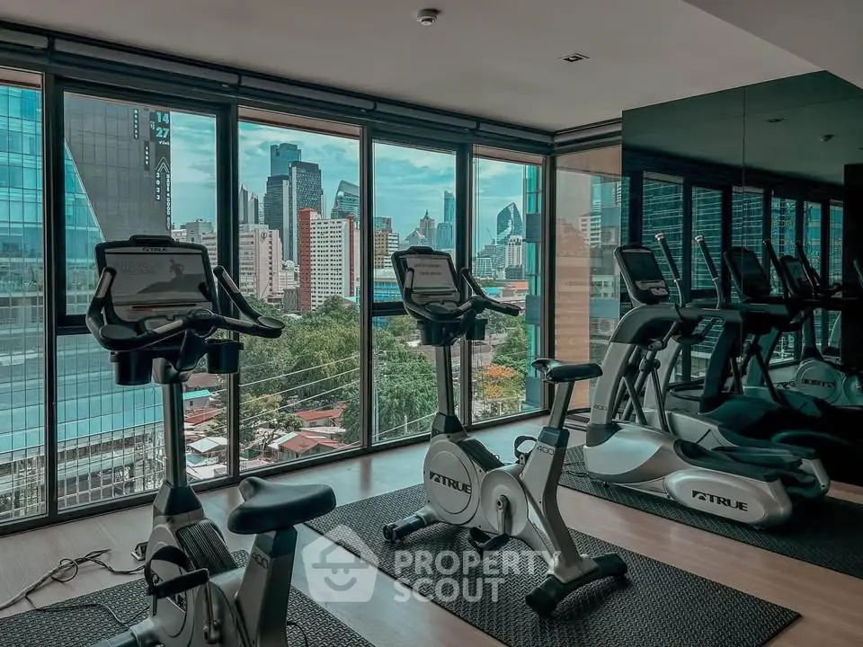 Modern gym with city view, featuring exercise bikes and floor-to-ceiling windows in a high-rise building.