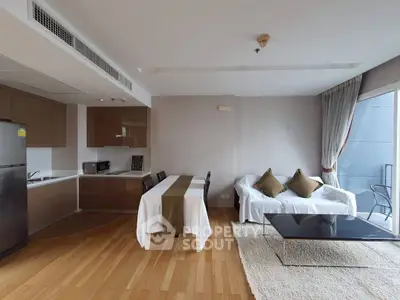 Modern open-layout living room with kitchen, featuring sleek furniture and wooden flooring.