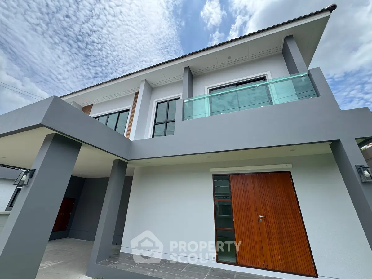 Modern two-story house with sleek design and glass balcony under a blue sky.