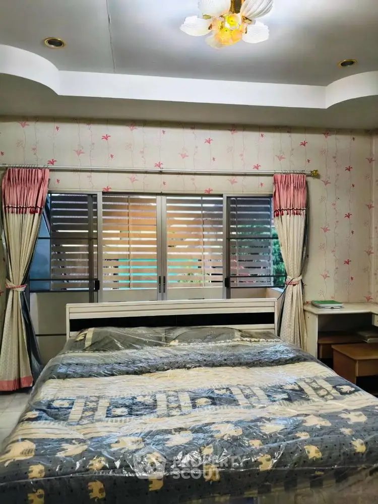 Cozy bedroom with floral wallpaper and large window, featuring a comfortable bed and elegant curtains.