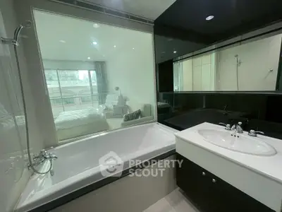 Modern bathroom with bathtub and glass wall overlooking bedroom in luxury apartment.