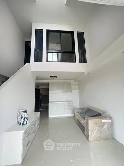 Modern loft-style living room with high ceiling and mezzanine, featuring sleek white cabinetry and tiled flooring.