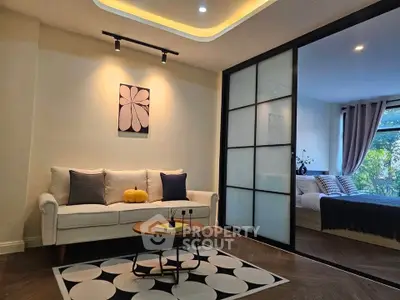 Modern living room with cozy sofa and stylish decor adjacent to a serene bedroom with large window view.