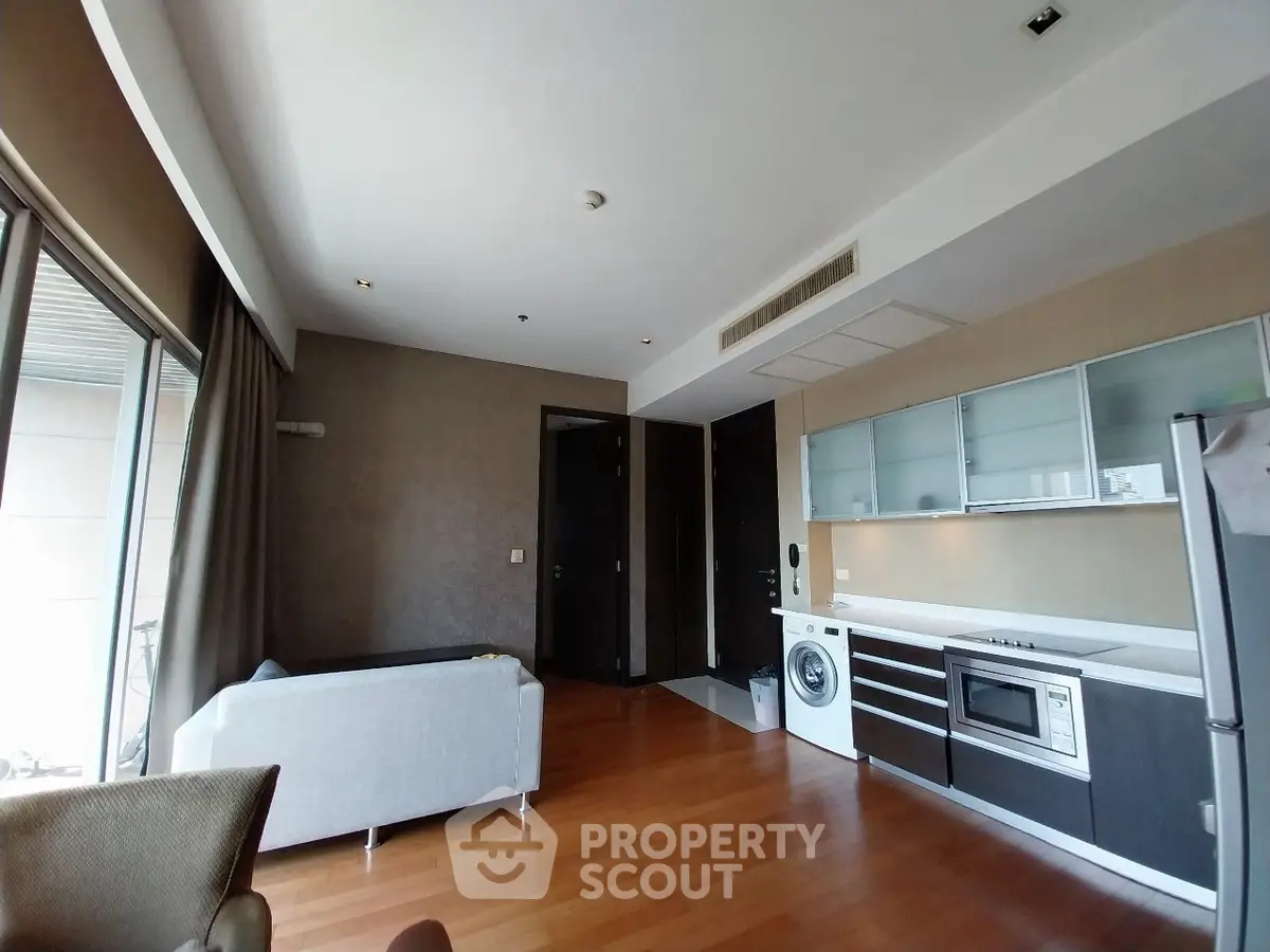 Modern living room with open kitchen, featuring sleek appliances and hardwood floors.