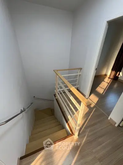 Modern staircase with wooden railing in a bright, sunlit interior space.