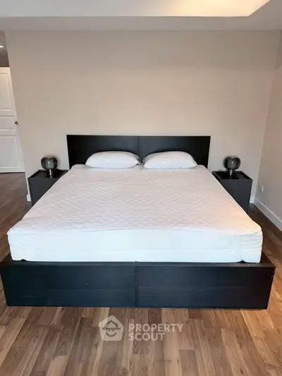 Spacious bedroom with modern black bed frame and hardwood flooring, perfect for a cozy retreat.