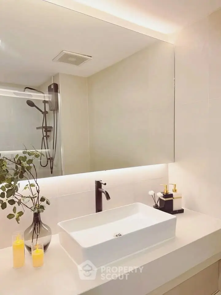 Modern bathroom with sleek sink and large mirror, featuring elegant decor and ambient lighting.