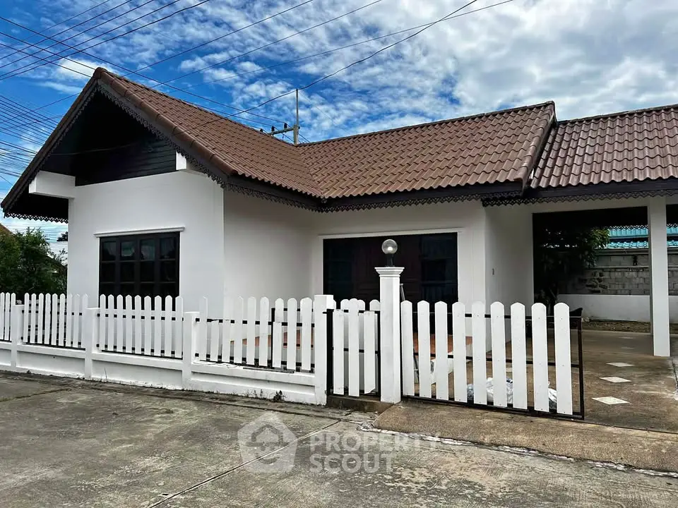 Charming single-story home with tiled roof and white picket fence under a vibrant blue sky.