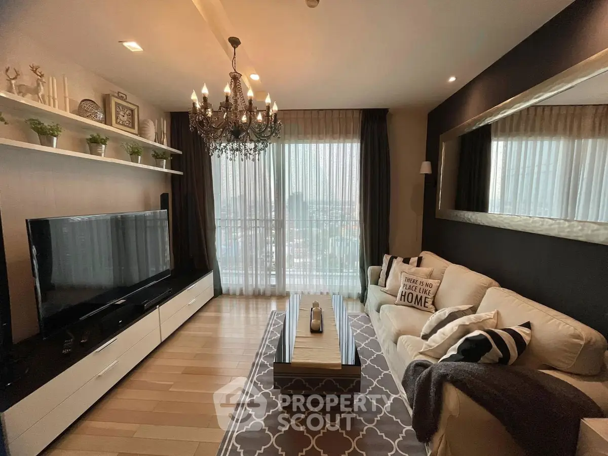 Elegant living room with chandelier, large TV, and cozy decor in modern apartment.