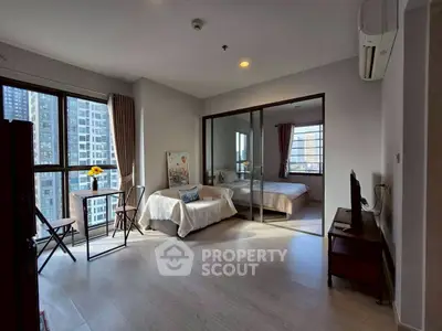 Modern apartment with open living room and bedroom, featuring large windows and city views.