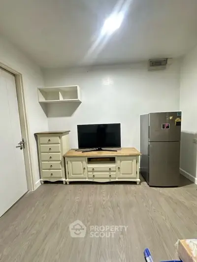Modern living room with TV, fridge, and stylish furniture in a cozy apartment.