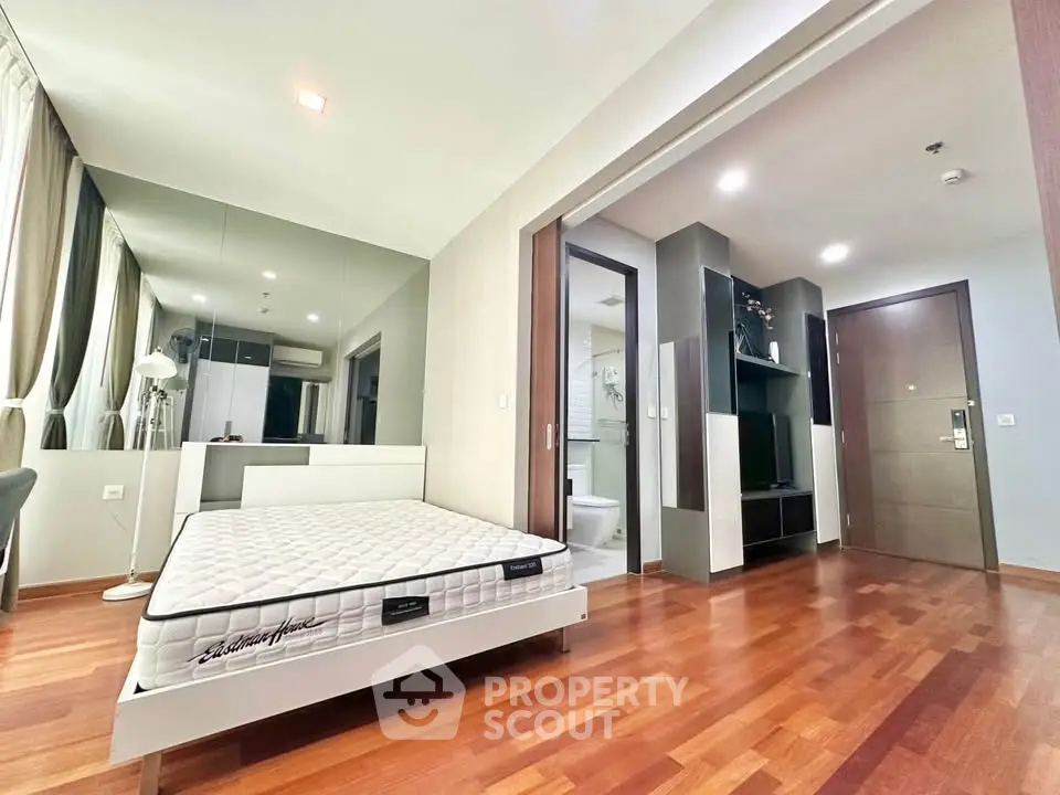 Modern bedroom with hardwood floors, mirrored wall, and ensuite bathroom in a stylish apartment.