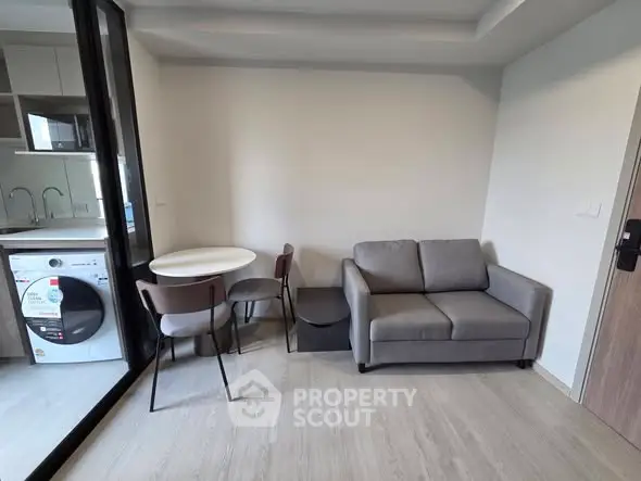 Modern living room with compact kitchen and washing machine in open layout.