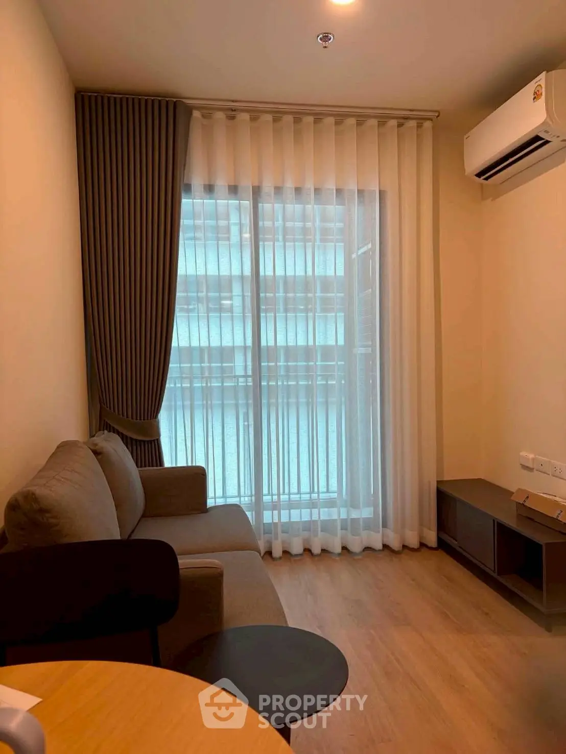 Cozy living room with modern sofa and air conditioning, featuring floor-to-ceiling windows and elegant curtains.