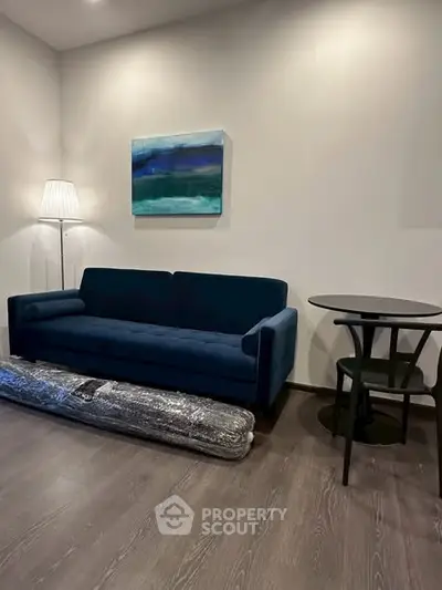Modern living room with stylish blue sofa, elegant floor lamp, and contemporary art on the wall.