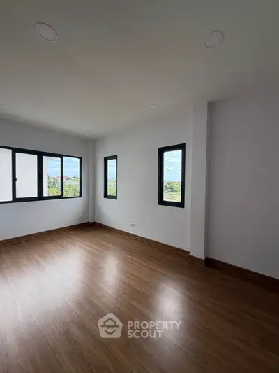 Spacious empty room with large windows and wooden flooring, offering a bright and airy atmosphere.