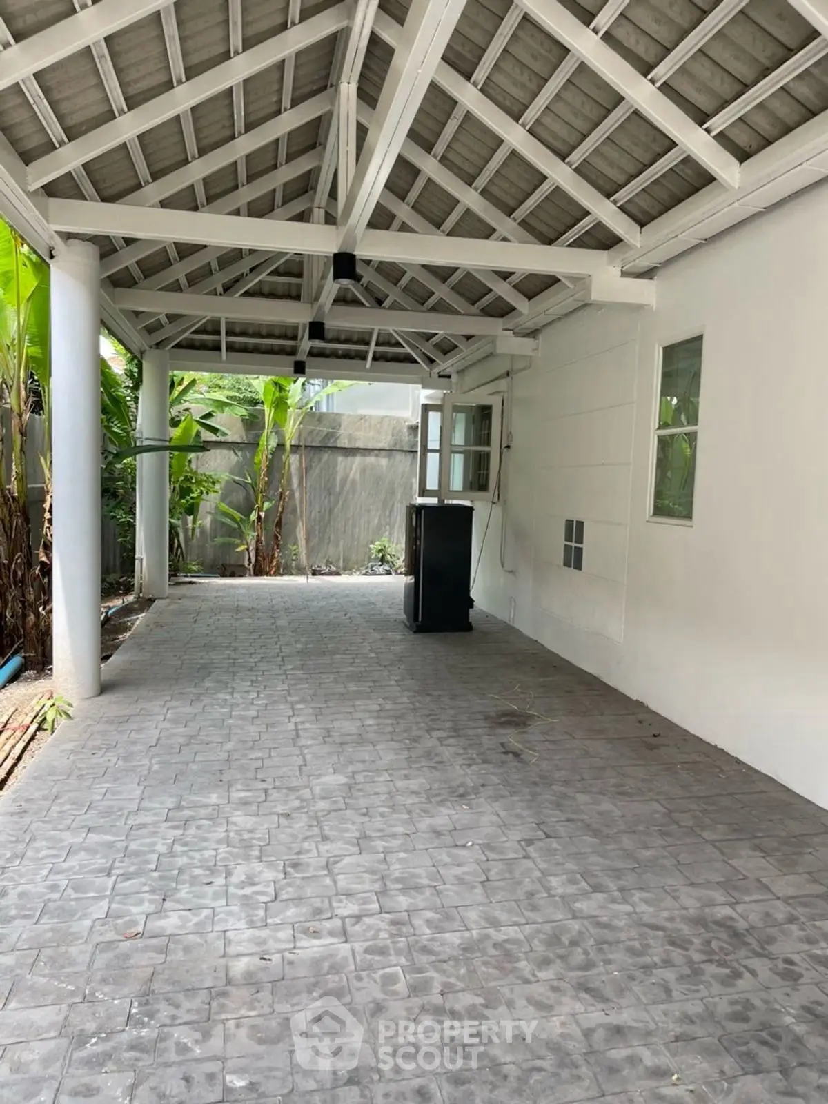 Spacious covered outdoor area with tiled flooring and garden view, perfect for parking or entertaining.