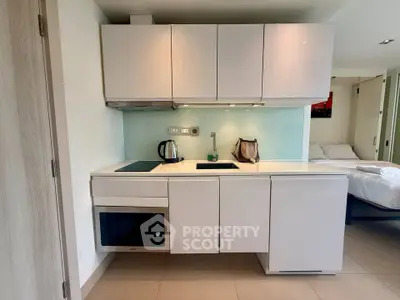 Modern compact kitchen with sleek white cabinets and built-in appliances in a cozy apartment.