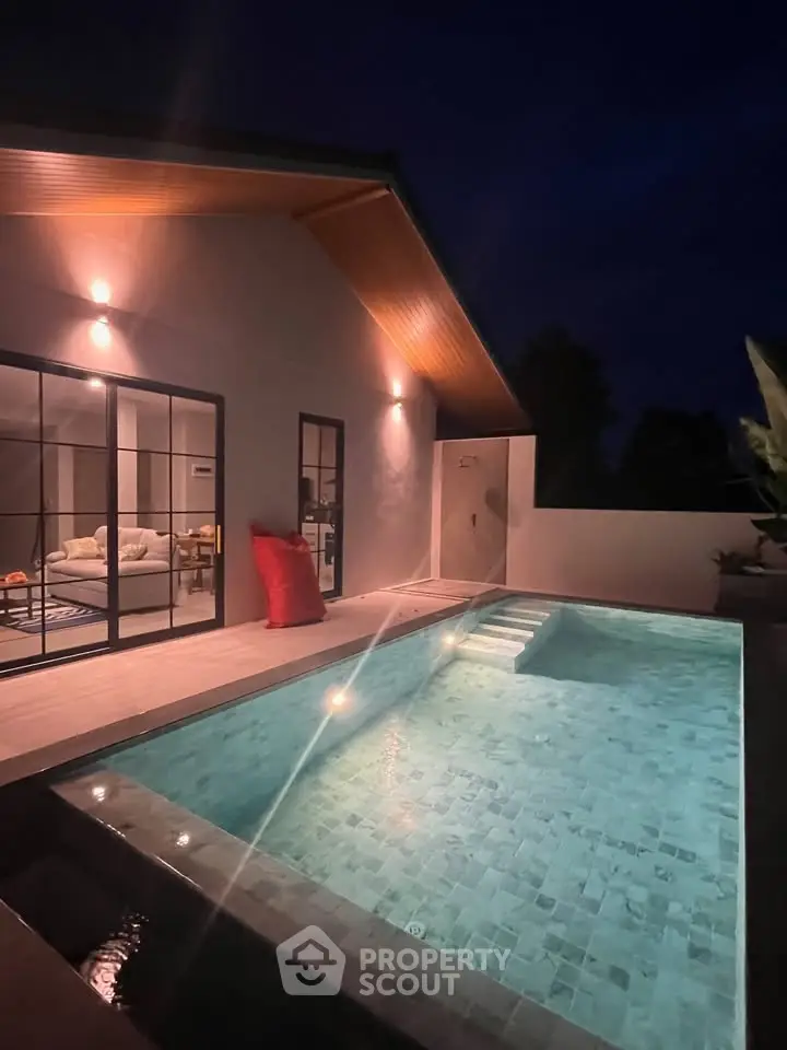 Luxurious modern home with illuminated pool and cozy interior view at night.