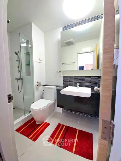 Modern bathroom with glass shower, sleek fixtures, and vibrant red rugs.