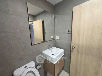 Modern bathroom with sleek sink and large mirror, featuring neutral gray tiles and wooden accents.