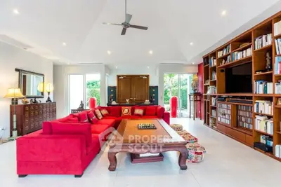 Luxurious living room with red sectional sofa, elegant wooden furniture, and built-in bookshelves.