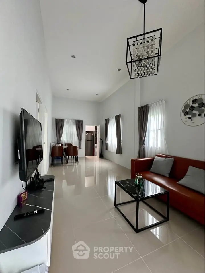 Modern living room with high ceiling, sleek furniture, and natural light.