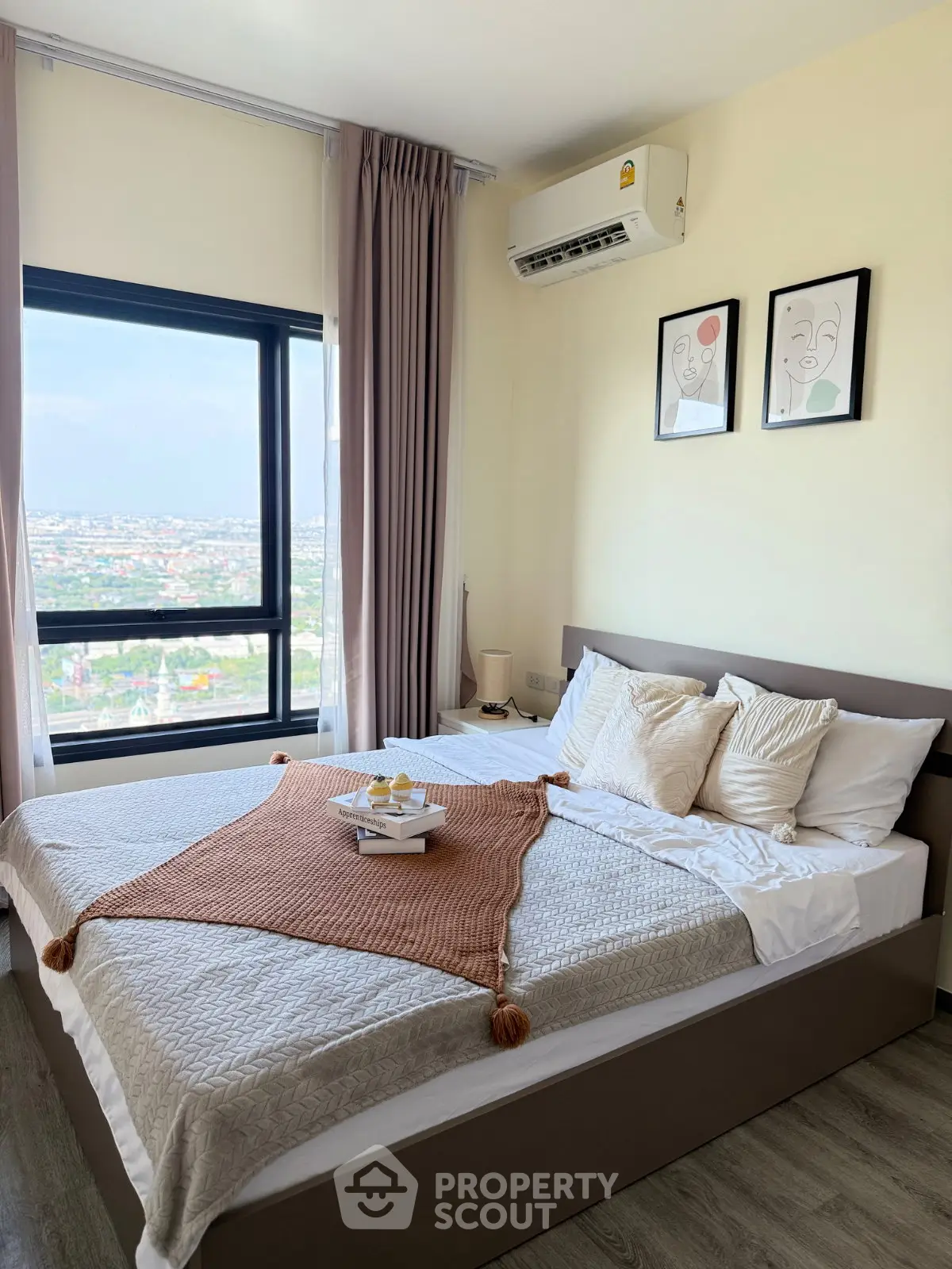 Modern bedroom with large window offering stunning city views, stylish decor, and cozy bedding.