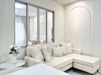 Elegant living room with modern beige sofa and decorative pillows, featuring a stylish partition window.