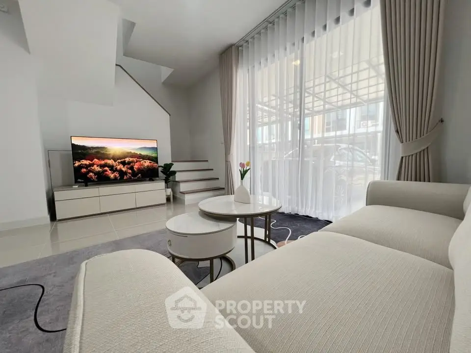 Modern living room with elegant decor, large TV, and natural light from floor-to-ceiling windows.