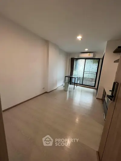 Spacious unfurnished living room with wooden flooring and large window leading to balcony.