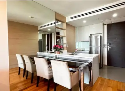 Modern dining area with sleek table and chairs, mirrored wall, and contemporary kitchen in open layout.