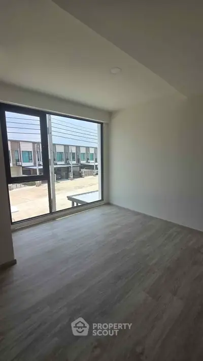 Spacious empty room with large window offering a view of modern townhouses, perfect for customization.