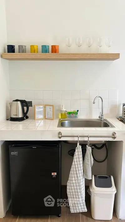 Compact kitchen with mini fridge, sink, and colorful glassware on shelf