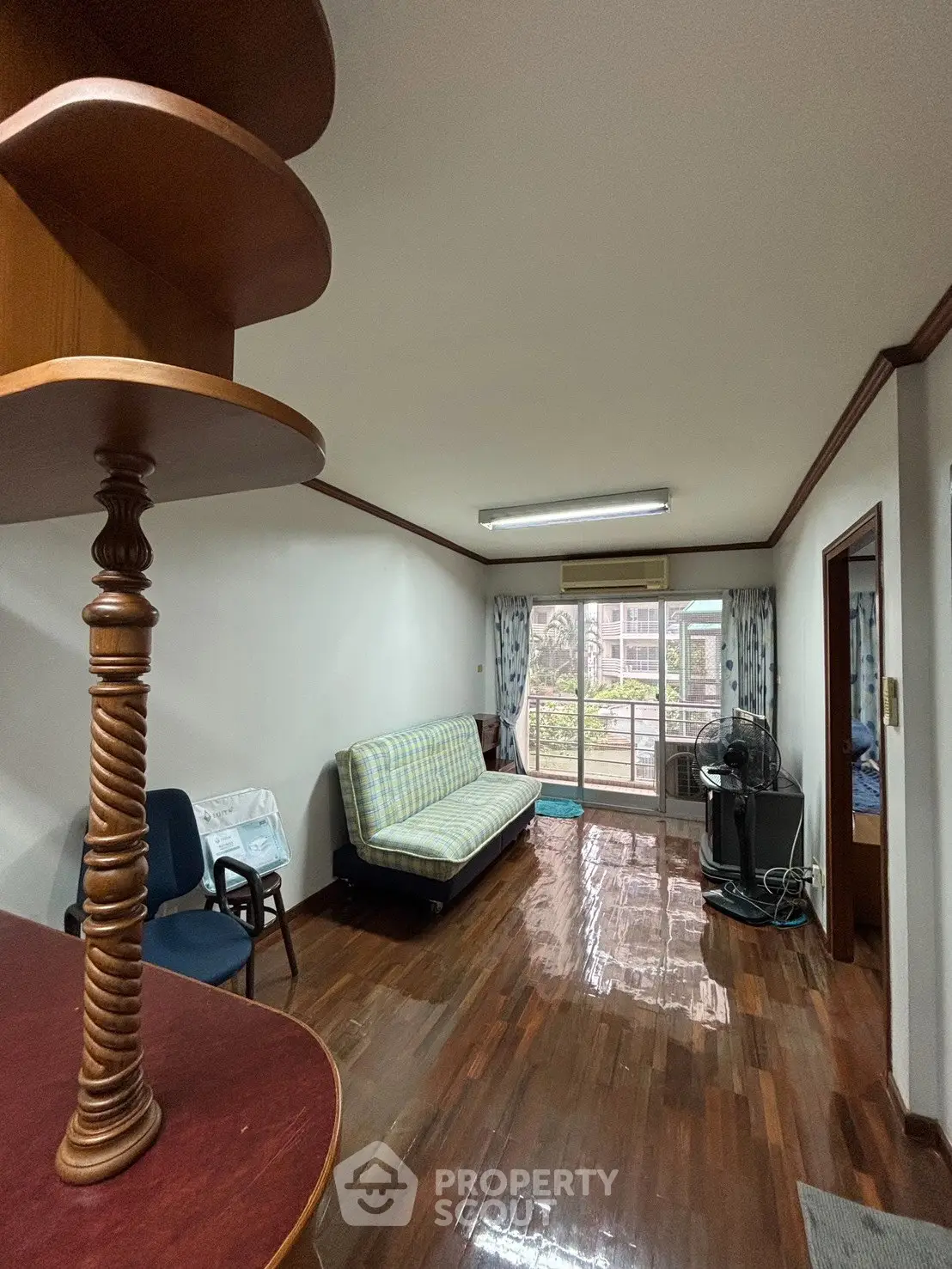 Spacious living room with wooden floors and balcony access in a cozy apartment.