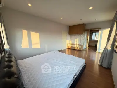 Spacious bedroom with wooden flooring and ample natural light in modern apartment.
