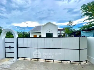 Modern white gate with archway leading to a stylish suburban home under a clear blue sky.